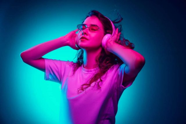 Caucasian woman’s portrait isolated on blue studio background in multicolored neon light