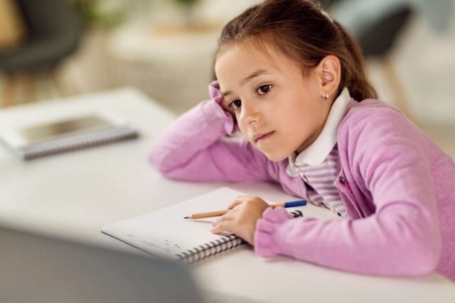Pensive little girl doing homework and learning at home.